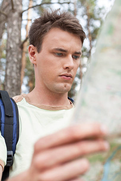 atractivo hombre joven con una mochila lectura mapa en el bosque - map uk hiking reading fotografías e imágenes de stock