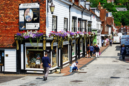Lewes, England - July 28, 2014: Harveys Brewery Shop on Cliffe High Street in Lewes, East Sussex, England. People walking along picturesque downtown street. Girl contemplating drain cover.