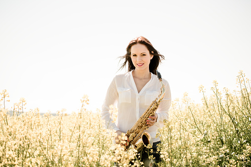 Portrait of young  saxophonist with her saxophone in blossoming rapeseed field