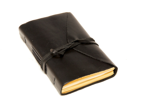 An old fashioned leather bound blank journal closed with cord wrapped around it, shot over white.