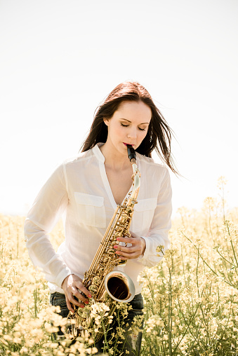 Passion - young  woman playing saxophone in blossoming rapeseed field