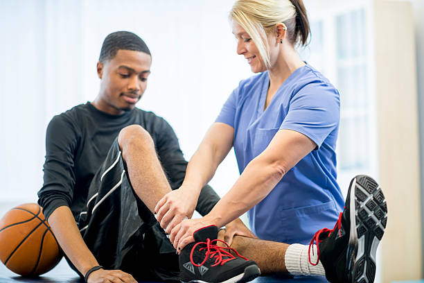 Basketball Player Getting Physical Therapy A male teenage basketball player is at the doctors office to have some work done on his injury. A physical therapist is working with him on his injury. team sport photos stock pictures, royalty-free photos & images