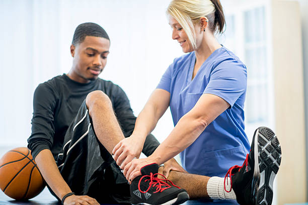 Basketball Player Getting Physical Therapy A male teenage basketball player is at the doctors office to have some work done on his injury. A physical therapist is working with him on his injury. sports physical stock pictures, royalty-free photos & images