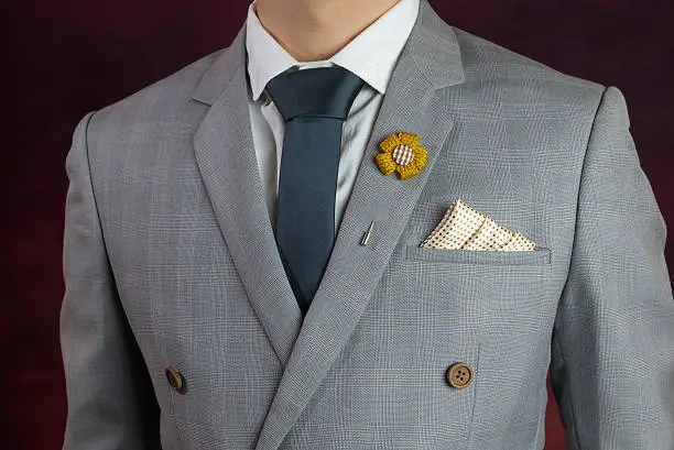 Man in grey suit, plaid texture, blue necktie, flower brooch, and dot pattern handkerchief, close up