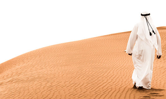An Arab man walking on the dunes of Dubai, United Arab Emirates. Wide & High Contrast Composition.