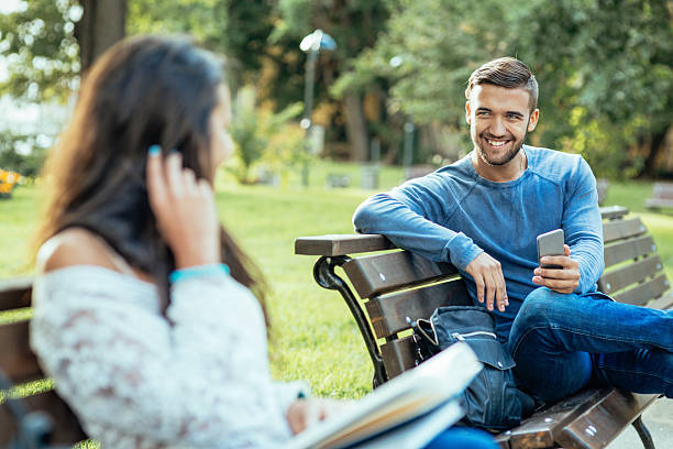 Girl and boy flirting Boy texting on cell phone and smiling to young girl who is reading book flirty stock pictures, royalty-free photos & images