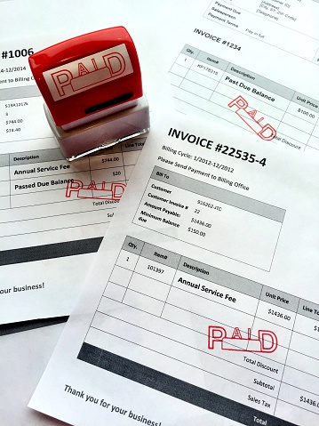 stack of invoices have been paid and marked paid by a red rubber stamp. some of the invoices contained a passed due balance. 