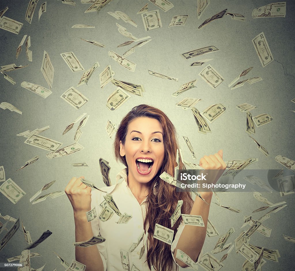 woman pumping fists celebrates success under money rain Portrait happy woman exults pumping fists ecstatic celebrates success under a money rain falling down dollar bills banknotes isolated on gray wall background with copy space Currency Stock Photo
