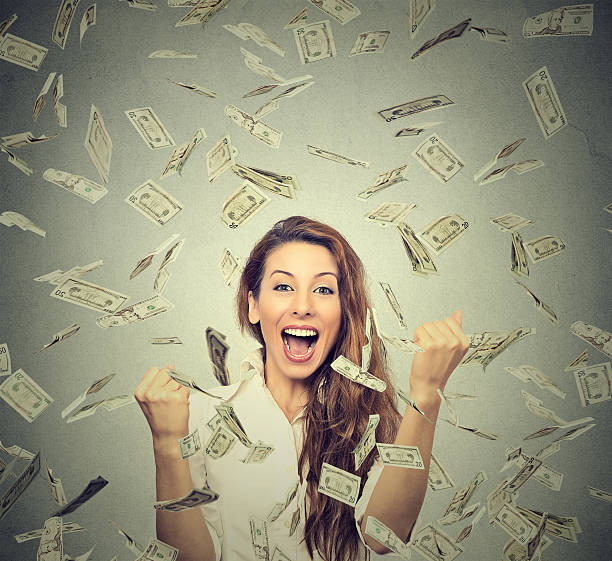 woman pumping fists celebrates success under money rain Portrait happy woman exults pumping fists ecstatic celebrates success under a money rain falling down dollar bills banknotes isolated on gray wall background with copy space free bingo stock pictures, royalty-free photos & images