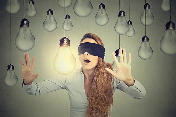 Blindfolded young woman walking through lightbulbs searching bright idea