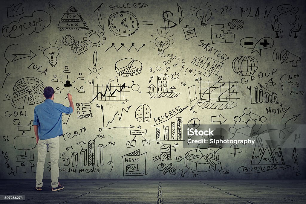 Business man entrepreneur writing new project calculations Business man young entrepreneur writing some new project calculations on gray wall Science Stock Photo