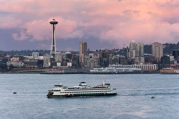 A ferryboat crosses Elliott Bay in front of the Seattle skyline and the historic Space Needle which is a leftover from the 1962 World's Fair during a lovely sunset.