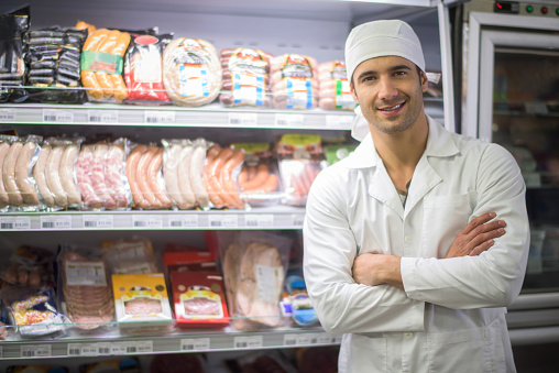 Latin American man working at the deli in the supermarket and standing next to a fridge with some products