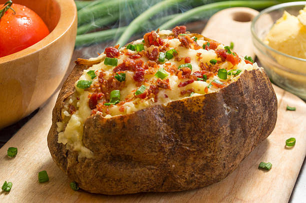 fresh hot baked potato fresh hot baked potato with butter bacon and chives on a cutting board baked potato stock pictures, royalty-free photos & images