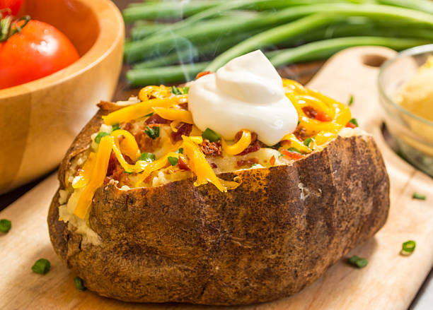 fresh hot baked potato fresh hot baked potato with butter bacon cheese and chives topped with sour cream on a cutting board Baked Potato stock pictures, royalty-free photos & images