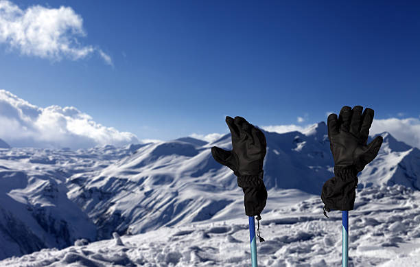 Gloves on ski poles and snowy mountain at sunny day