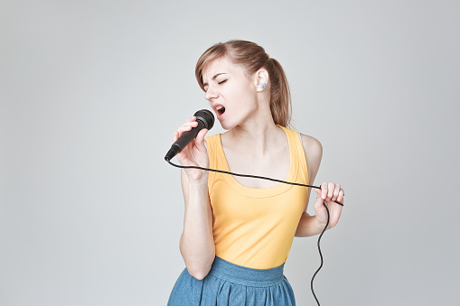 Beautiful young woman singing into a microphone karaoke showing expressions and feelings