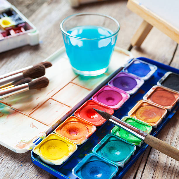 istock Watercolor paints, brushes and glass of water on old table 507374500