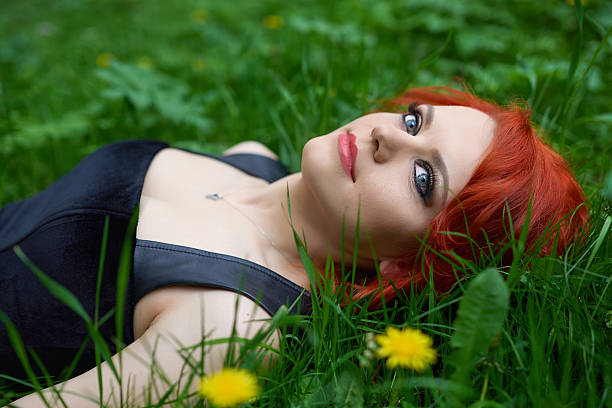 alone with my thoughts side view of young woman lying in the grass, looking away and day dreaming, red hair, eye makeup. women lying down grass wood stock pictures, royalty-free photos & images