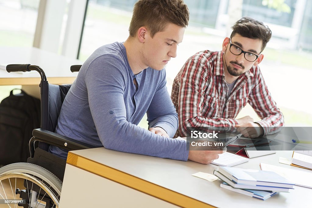 College Student in Wheelchair at Library College student in wheelchair learning with friend. Wheelchair Stock Photo