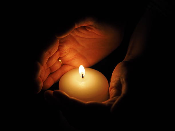 istock candle and hands on a black background 507402556
