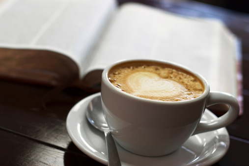 A coffee cup in front of a bible with shallow depth of field.