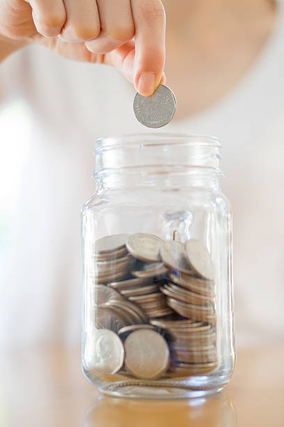 istock Woman Dropping Coins Into Glass Jar 507419212