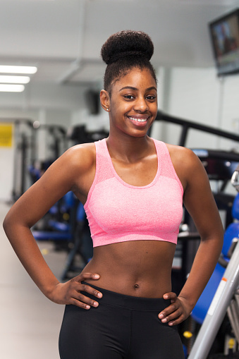 Young black woman posing in the gym with hands on hips and smiling at the camera.