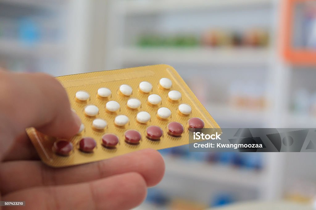 Close up of pharmacist hands holding contraceptive pills Close up of pharmacist hands holding contraceptive pills with pharmacy store shelves background Adult Stock Photo