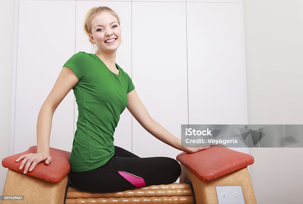 Girl in sportwear on relax massage equipment healthy spa salon Smiling blond girl in sportwear sitting on modern relax massage equipment. Young woman doing relaxation exercise in healthy spa salon. Alternative Therapy Stock Photo
