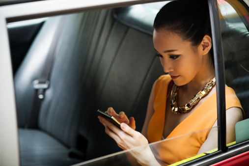 Young businesswoman in Hong Kong taxi, using smartphone.