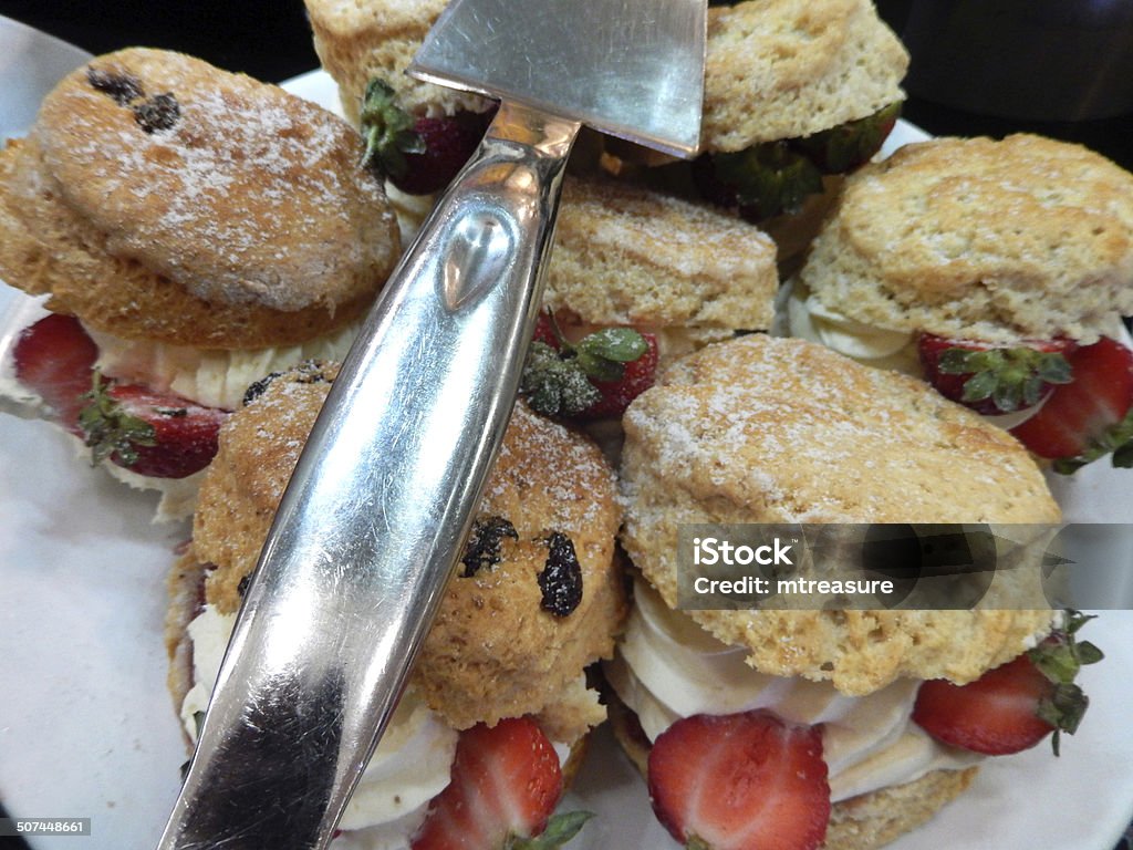 Image of cream scones with strawberries, cream tea cakes, afternoon-tea Photo showing an indulgent plate of luxury homemade cream scones, ready for a cream tea at an afternoon tea party.  The scones are pictured with a silver cake slice and displayed on a white plate.  A traditional cream tea (also referred to as a Devonshire, Devon or Cornish cream tea) consists of scones and clotted cream. Afternoon Tea Stock Photo