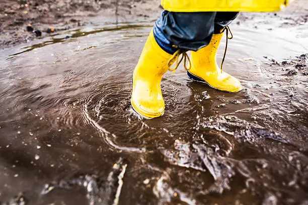 Child Wearing Yellow Rainboots Playing in Puddle after rain