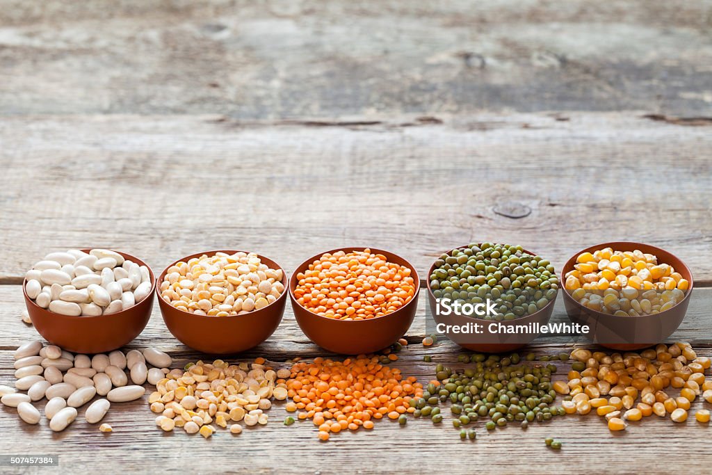 Cereal grains: red lentils, green mung, corn, bean and peas Bowls of cereal grains: red lentils, green mung, corn, beans and peas on wooden table. Green Pea Stock Photo