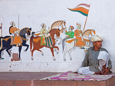 Rohet, India - March 9, 2015: Unidentified man sitting in front of street art containing a level of detail typically found in the Rajasthani painting tradition 