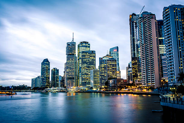 Long exposure shot of Brisbane skyline at dusk. There are some skyscrapers in back and river in front. Lights in offices and appartments are turned on. City lights are reflecting in the river.