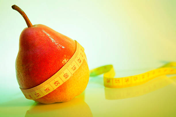 Close-up of a red pear with a measuring tape around it. Much space for copy. Shallow depth of field. Can illustrate the concept of dieting, weight loss, etc.