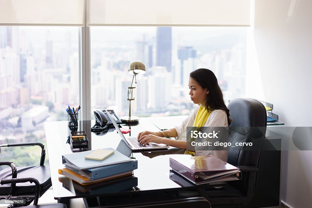 Business Woman Secretary Typing On Laptop Computer In Office Adult businesswoman sitting in modern office in skyscraper. The secretary writes on laptop pc with serious expression. Wide shot Computer Stock Photo