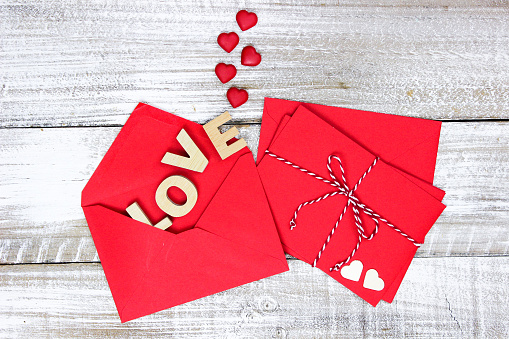 Red note cards tied in string by envelope with the word LOVE and hearts coming out on white rustic antique wooden background