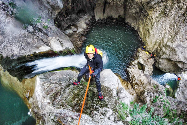 Moving down the waterfall Man with climbing equipment rappeling down the waterfall in the canyon. The other tteam members can be seen in the background. canyoneering stock pictures, royalty-free photos & images