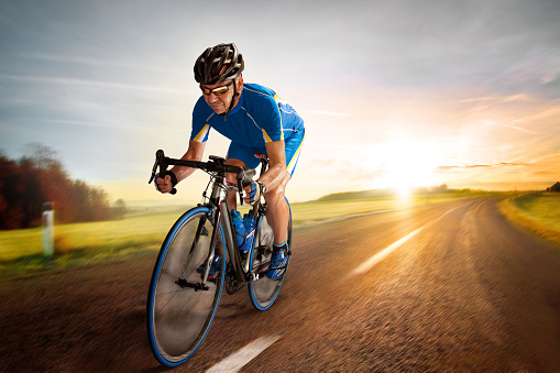 Close up photo of an active triathlete in sportswear and with a protective helmet riding a bicycle. Selective focus.