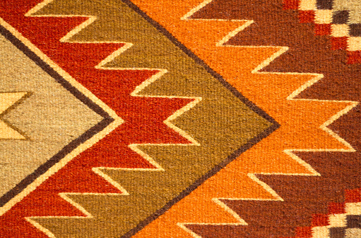A close-up detail of a vibrant orange-brown traditional geometric Mexican wool rug.