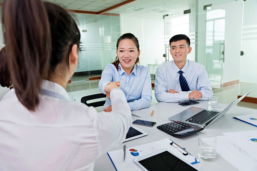 Three asian business people shaking hands at a conference table.