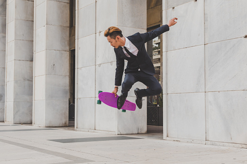 Young handsome Asian model dressed in dark suit and tie jumping with his skateboard