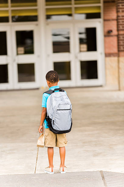 istock African descent, little boy faces school building. Lunch, backpack. 507510073