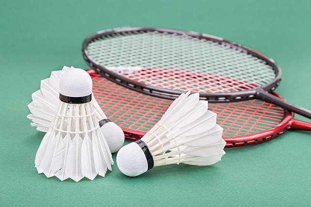istock Three new badminton shuttlecock with rackets on green mat court 507511302