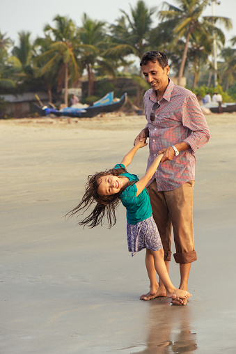 Asian father playing active outdoor games with his daughter on the bech. Happy mixed race family having fun on the beach at sunset.