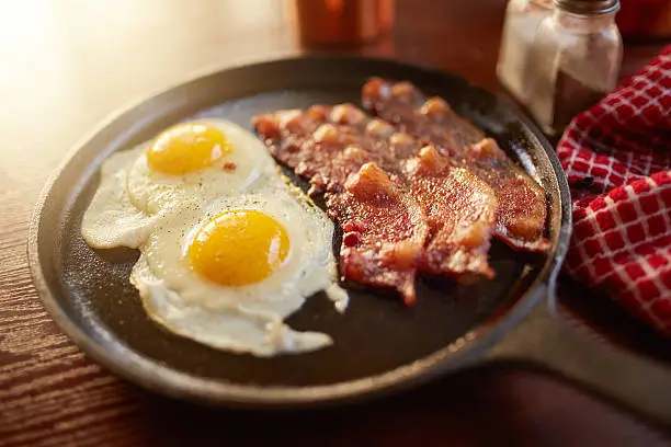 fried bacon and eggs in iron skillet shot with selective focus