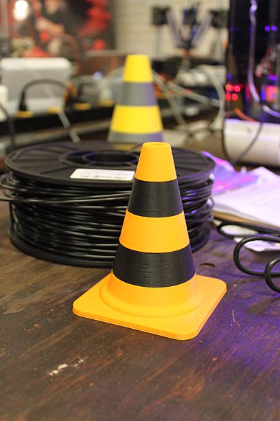 Black and yellow traffic cone Black and yellow traffic cone on desk, standing before a black spool of 3D printing filament polylactic acid stock pictures, royalty-free photos & images