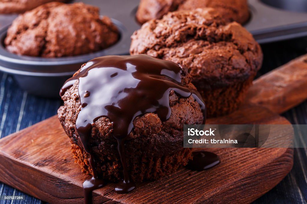 Chocolate muffins with chocolate syrup on dark background. Chocolate muffins with chocolate syrup on dark background, selective focus. Baked Stock Photo